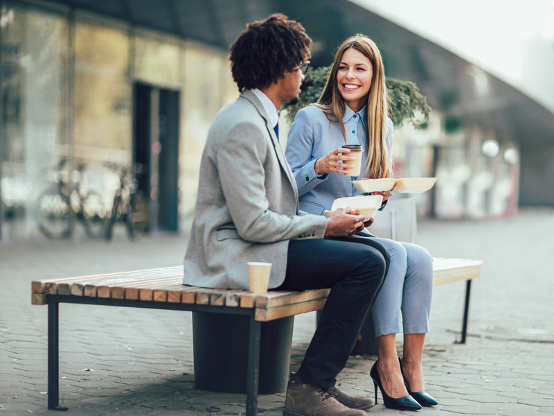 Business diners sitting on a bench sharing a meal